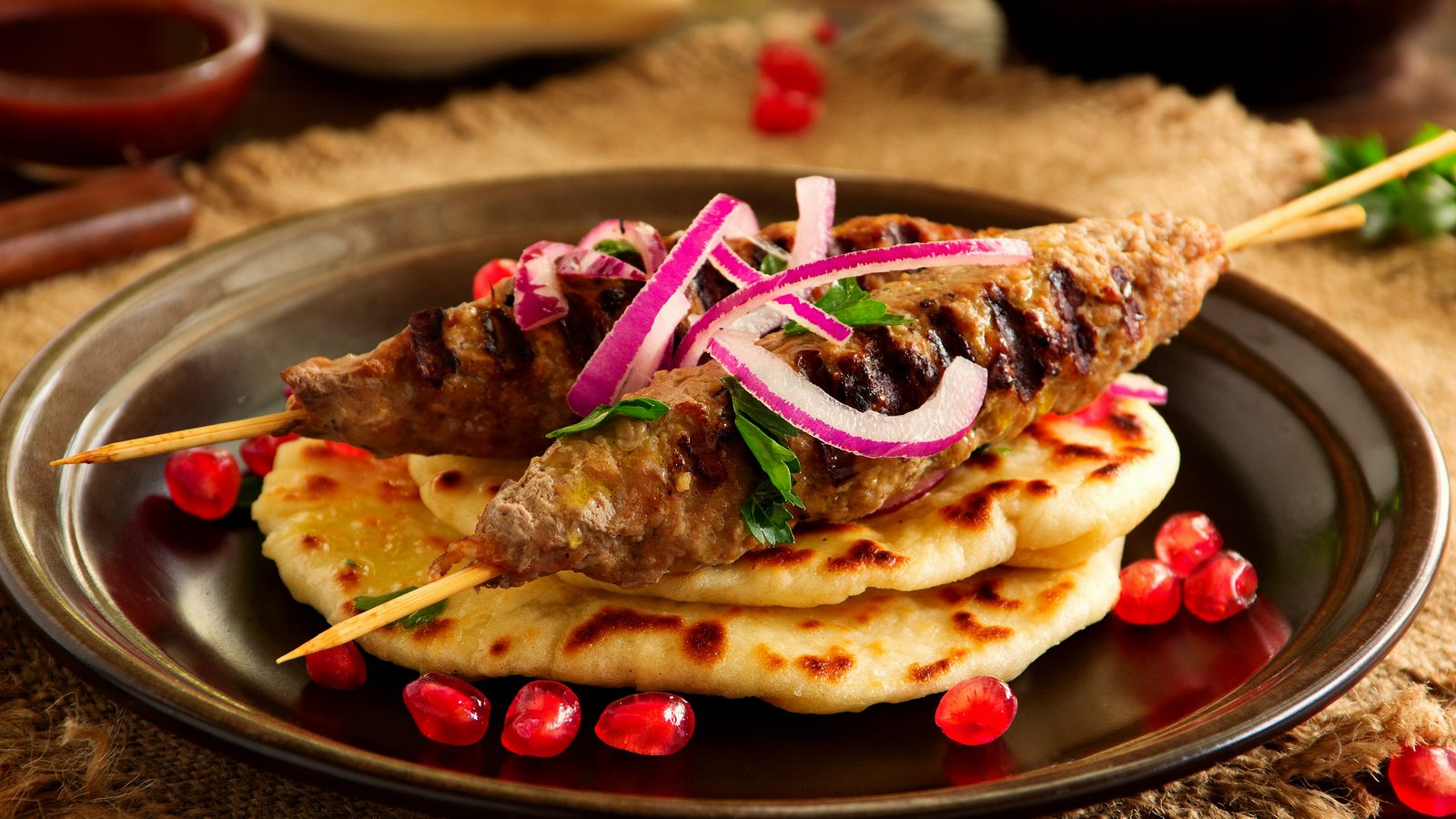 Grilled lamb kebab on flatbread with pomegranate and red onion