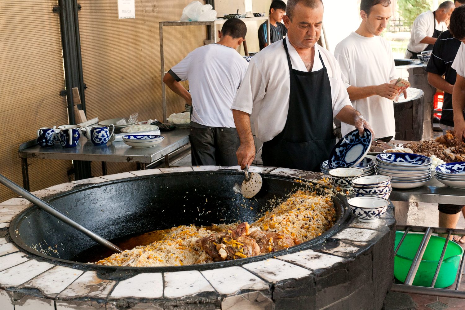 A cook stirring a full kazan of plov with a long paddle